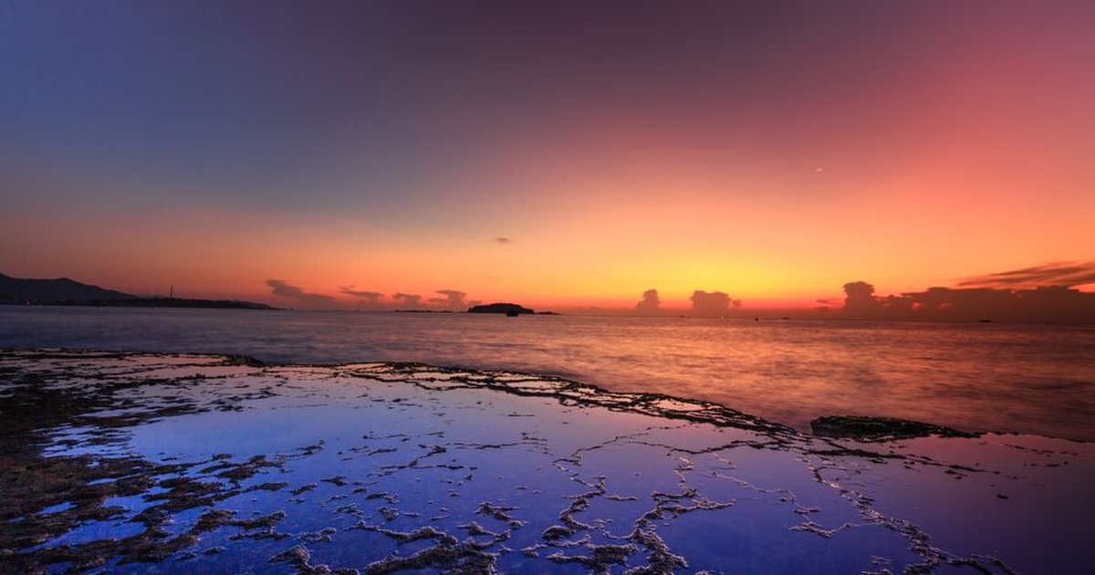 A breathtaking sunset over a tranquil seashore with reflective rocks and colorful sky.