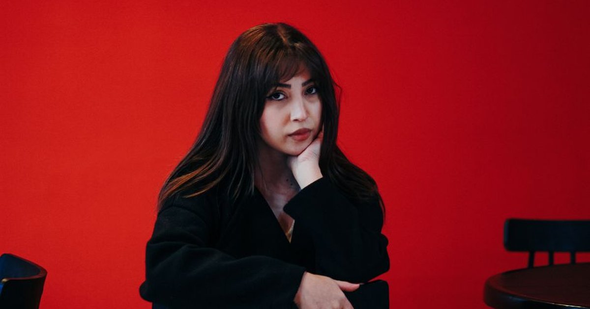 Stylish portrait of a young woman in a Tehran cafe, set against a bold red background.