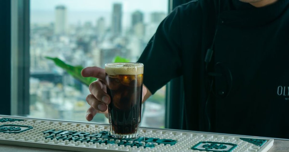 A barista serves a glass of iced coffee on a counter with a city skyline view.