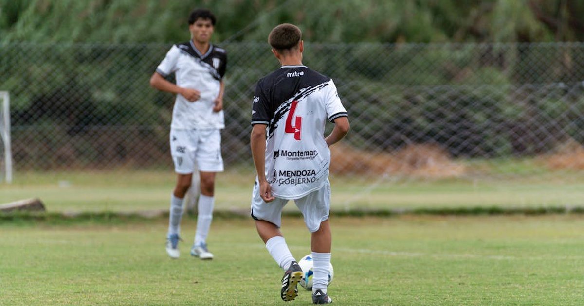 Two youths playing soccer on a grassy field, wearing team jerseys.