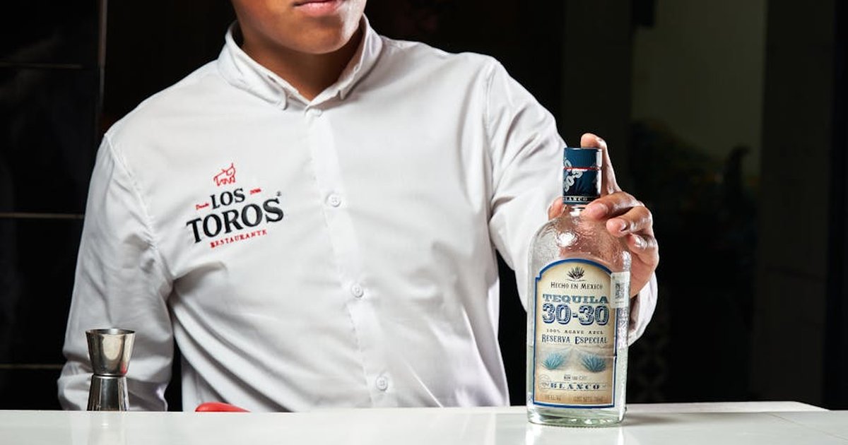 A bartender in Los Toros Restaurant displaying a bottle of Tequila 30-30, Reserva Especial.