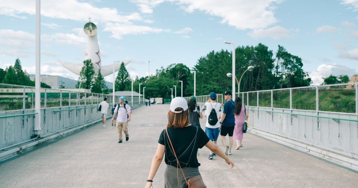 Woman in black t-shirt walking on bridge near Tower of the Sun.