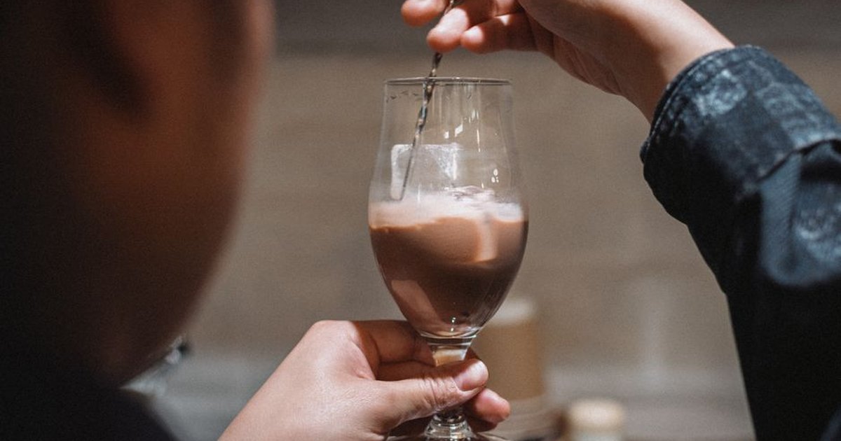 Barista stirring a creamy chocolate drink in a modern Tokyo cafe setting.