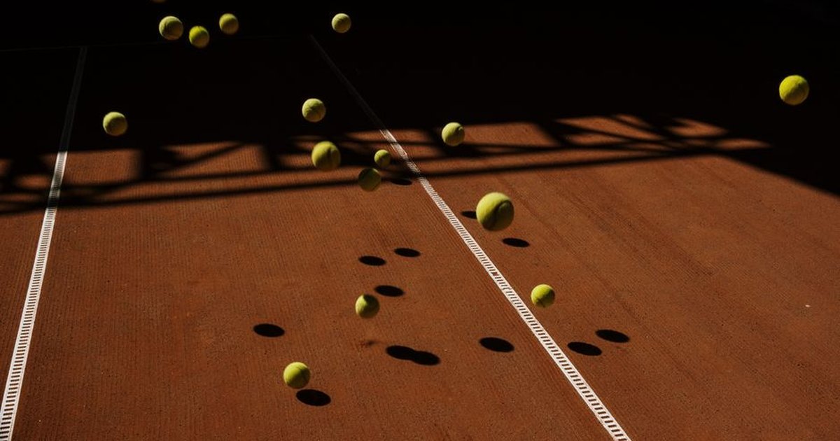 Artistic capture of tennis balls in motion casting dramatic shadows on a clay court surface.