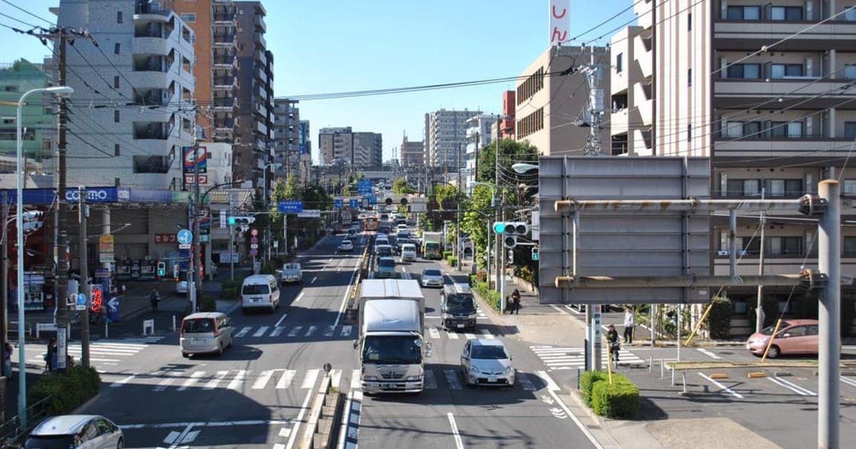 A bustling city street with vehicles, pedestrians, and tall buildings under clear blue skies.