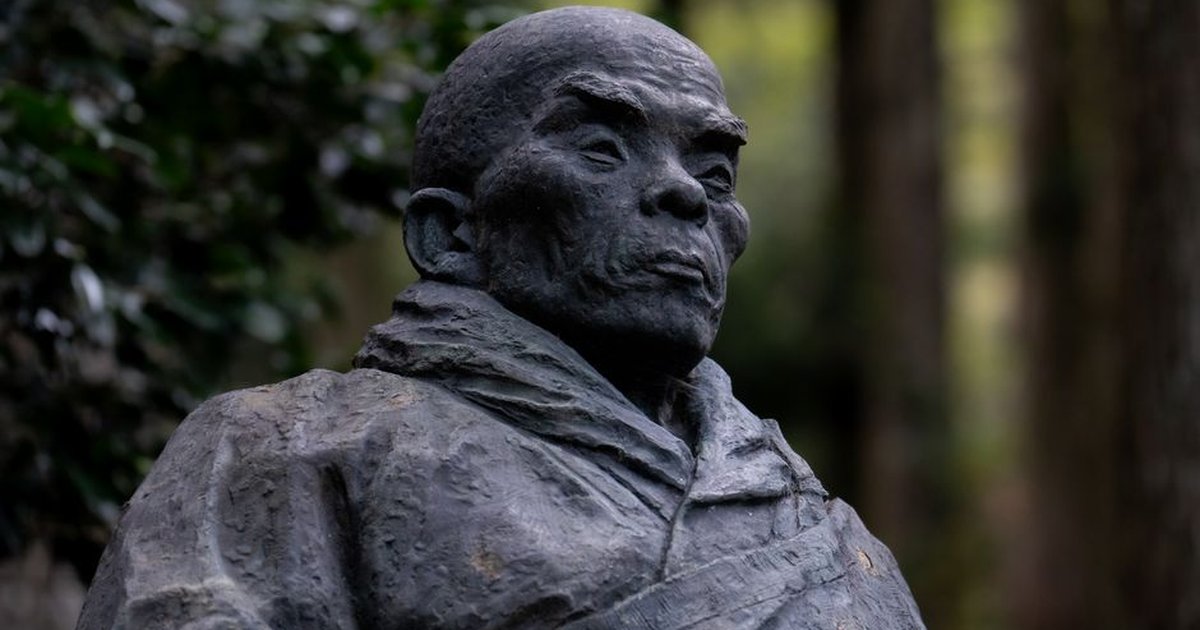 A close-up of a historic Japanese monk statue situated in a tranquil forest setting, capturing cultural essence.