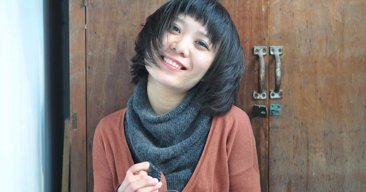 A cheerful woman in casual knitwear sits joyfully indoors.