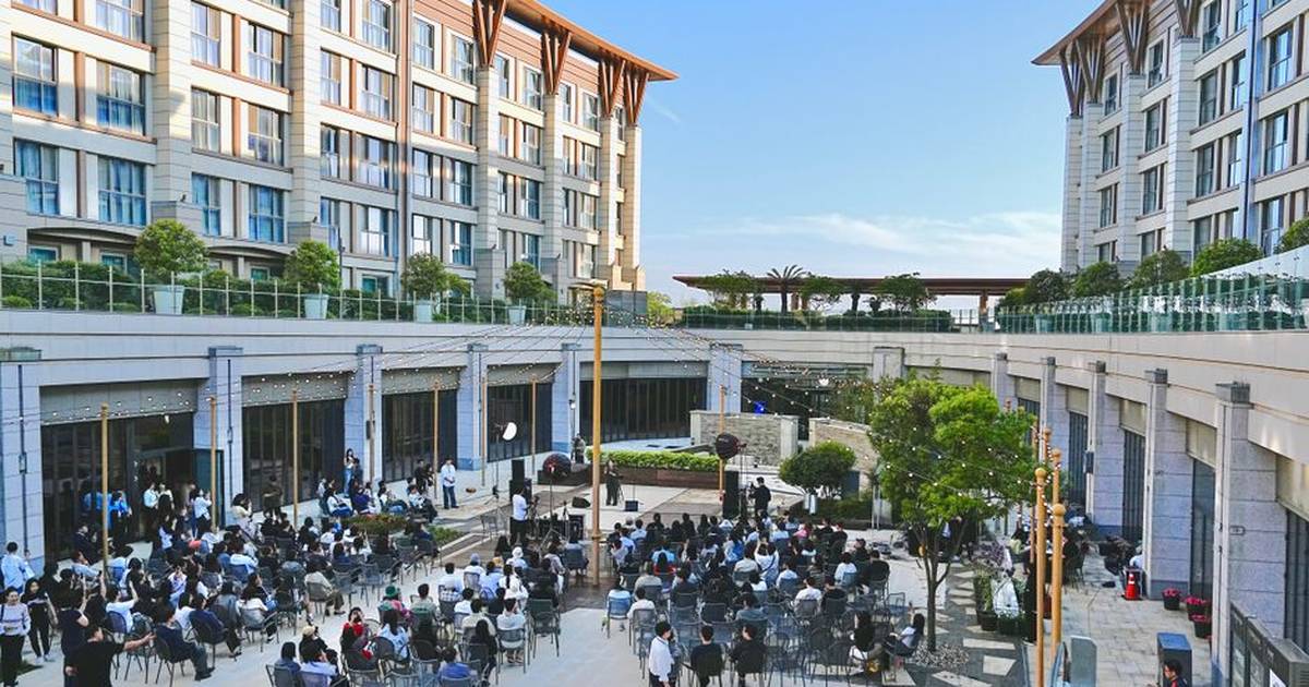 Large outdoor corporate event with attendees seated in courtyard of a modern building complex.