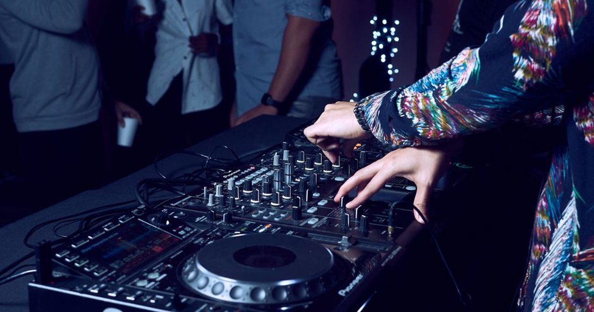 Hands of DJ adjusting audio mixer at a vibrant nightclub party.