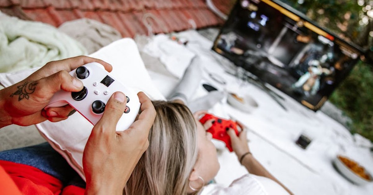 A couple playing video games outdoors, focusing on the controllers and screen.