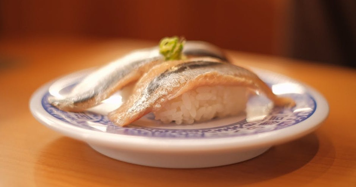 Close-up of fresh horse mackerel sushi served on a decorative porcelain plate with rice.