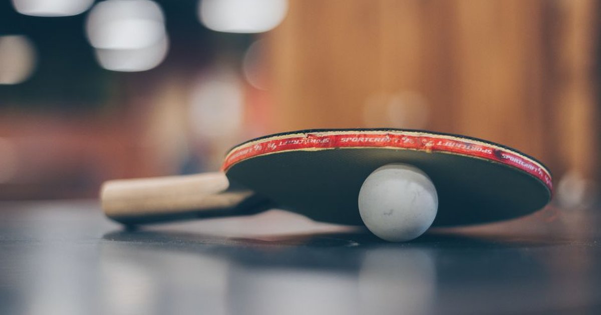 Close-up of a ping pong paddle and ball on a table with an artistic bokeh background, indoors.