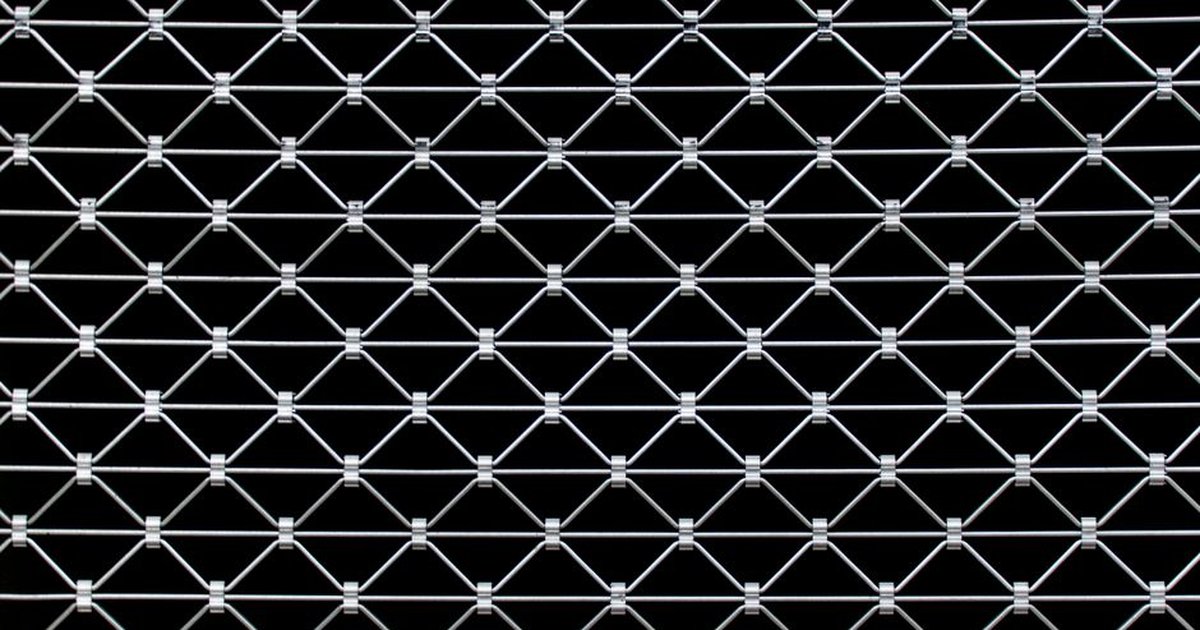 Close-up view of a symmetrical metal wire fence creating a geometric pattern against a dark background.
