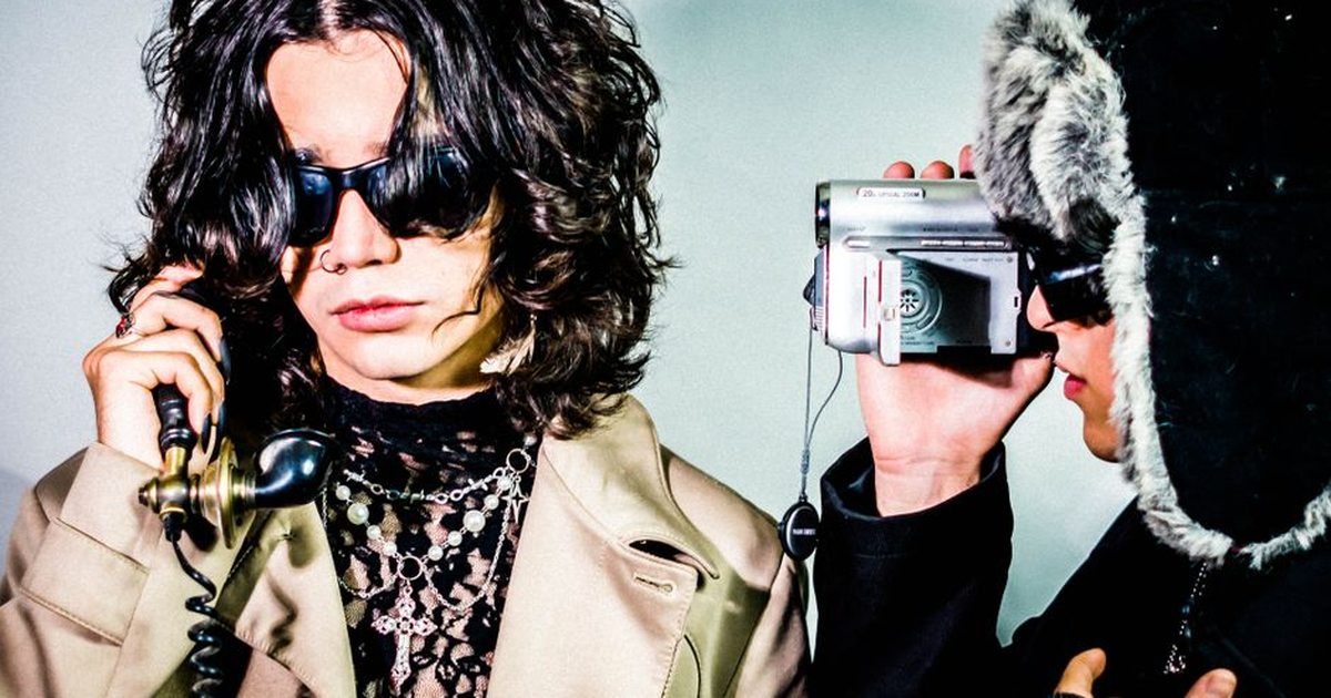 Two stylish adults posing with a vintage phone and camcorder in a retro, artistic setting.