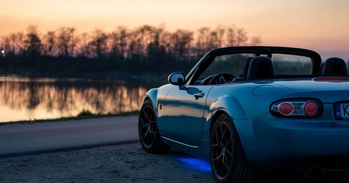 A sports car parked by a lake at sunset in Brzegi, Poland, offering a scenic view.