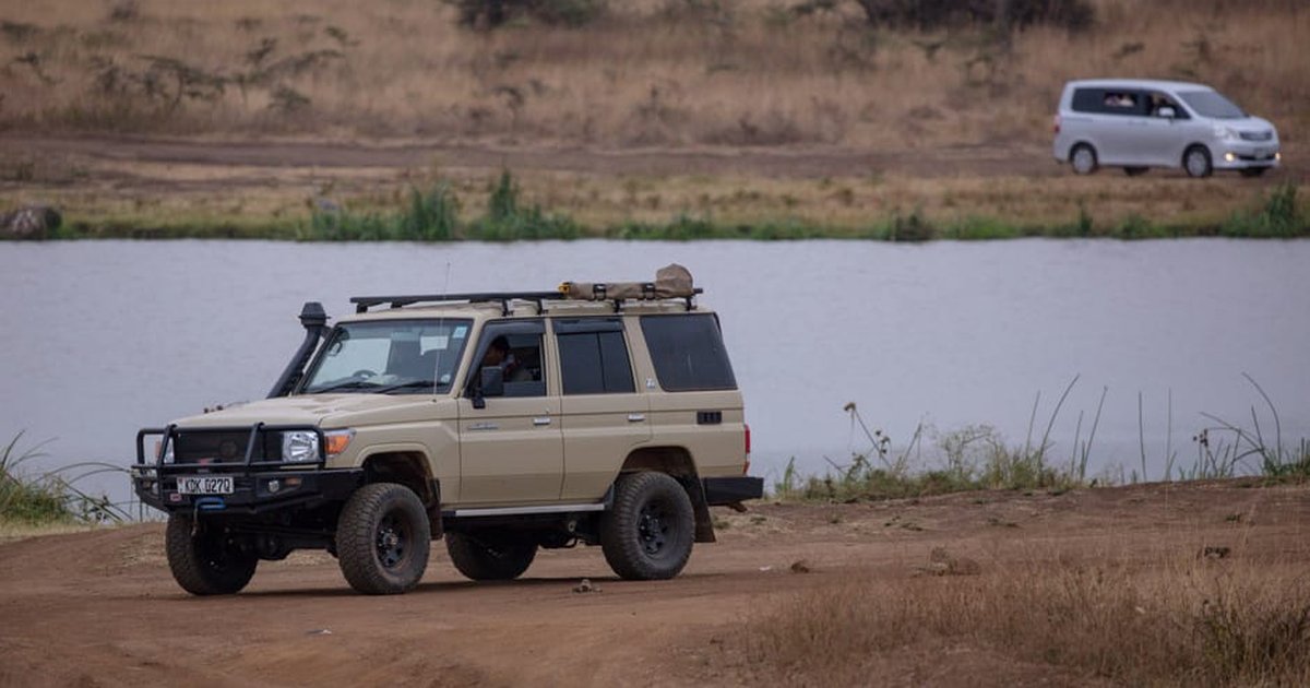 A safari vehicle parked by a serene lake in a vast African savanna landscape.