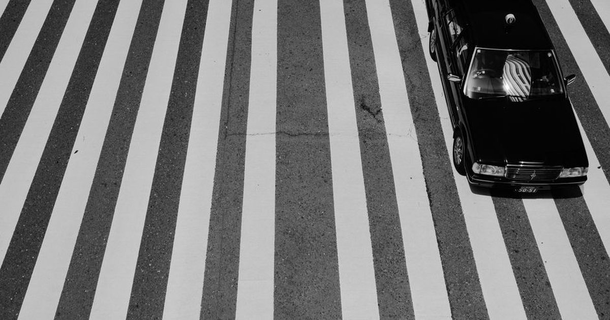 Black car on an urban crosswalk with bold lines, presenting a striking aerial view.