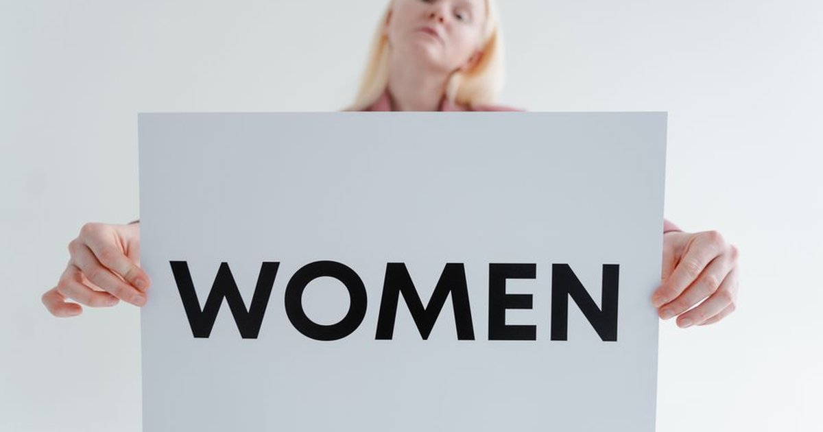 Confident woman holding a sign with the word 'WOMEN' in a bright studio setting.