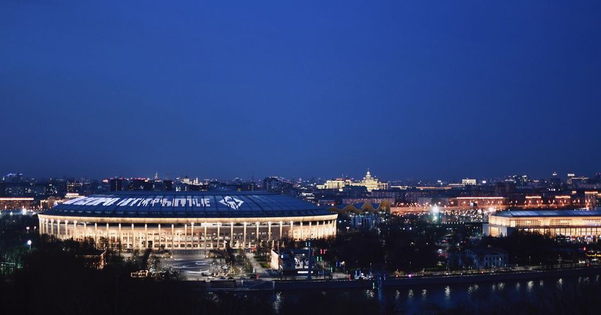 Breathtaking aerial view of Moscow's Luzhniki Stadium illuminated at twilight, with cityscape in the background.