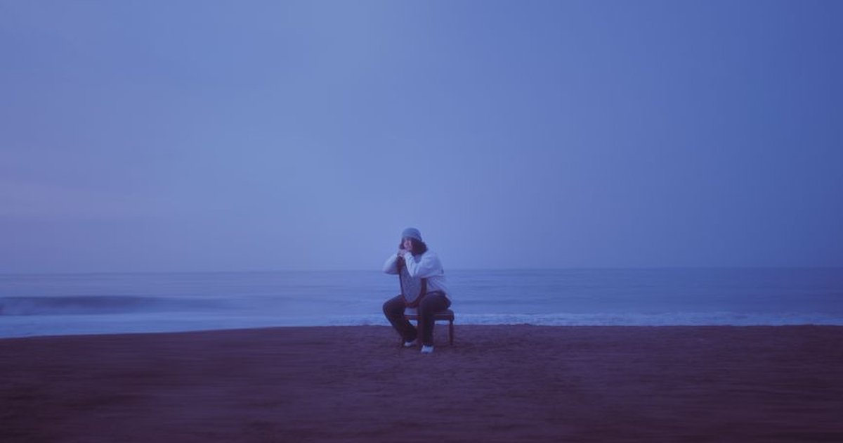 A person seated on the sand of Chorrillos Beach at dusk, Peru, reflecting quietly.