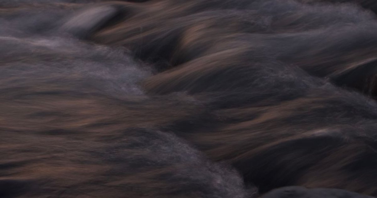 Close-up of a dark and wavy water stream captured at twilight, conveying serenity.