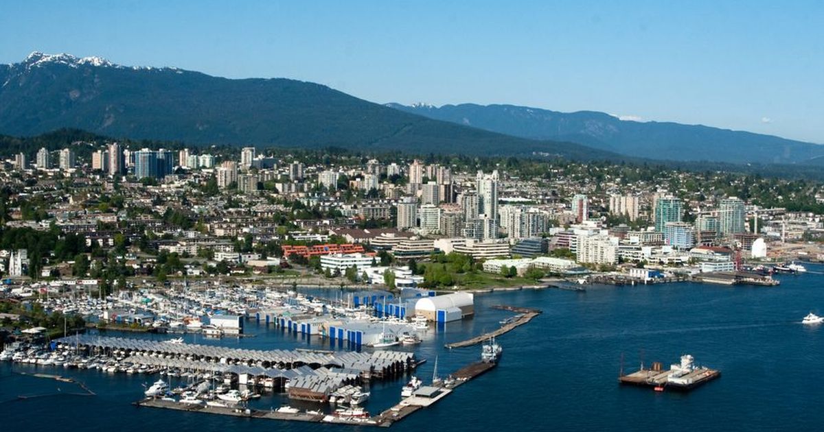 Scenic aerial view of a bustling coastal city with marina, mountains, and clear skies.