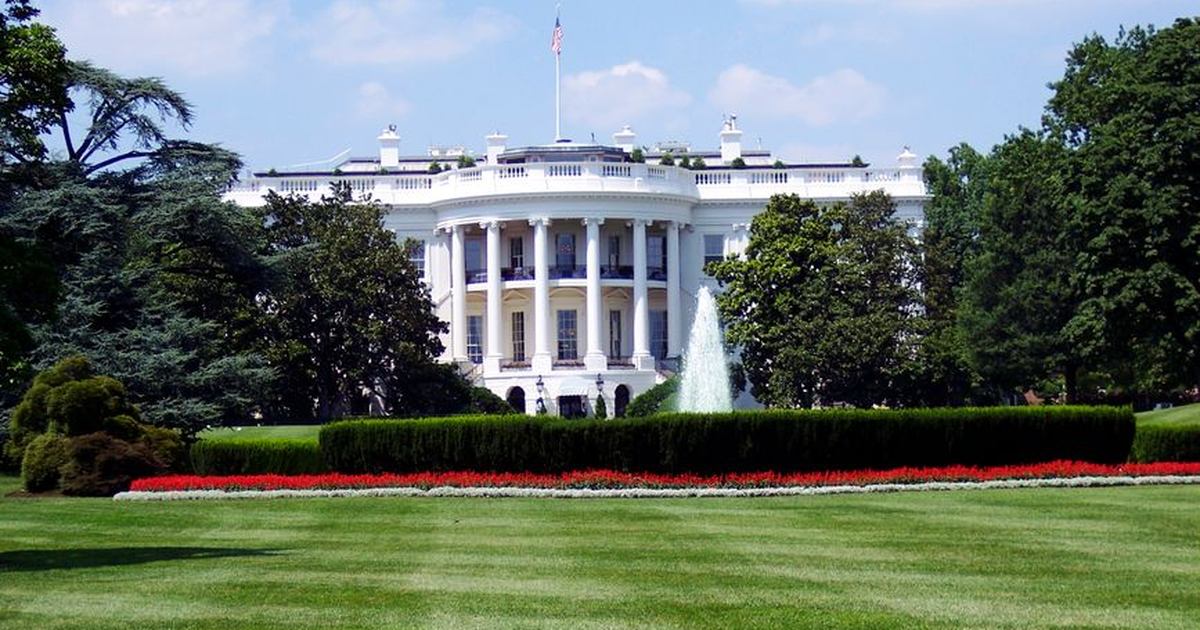 Iconic view of the White House with lush gardens and a central fountain on a sunny day.