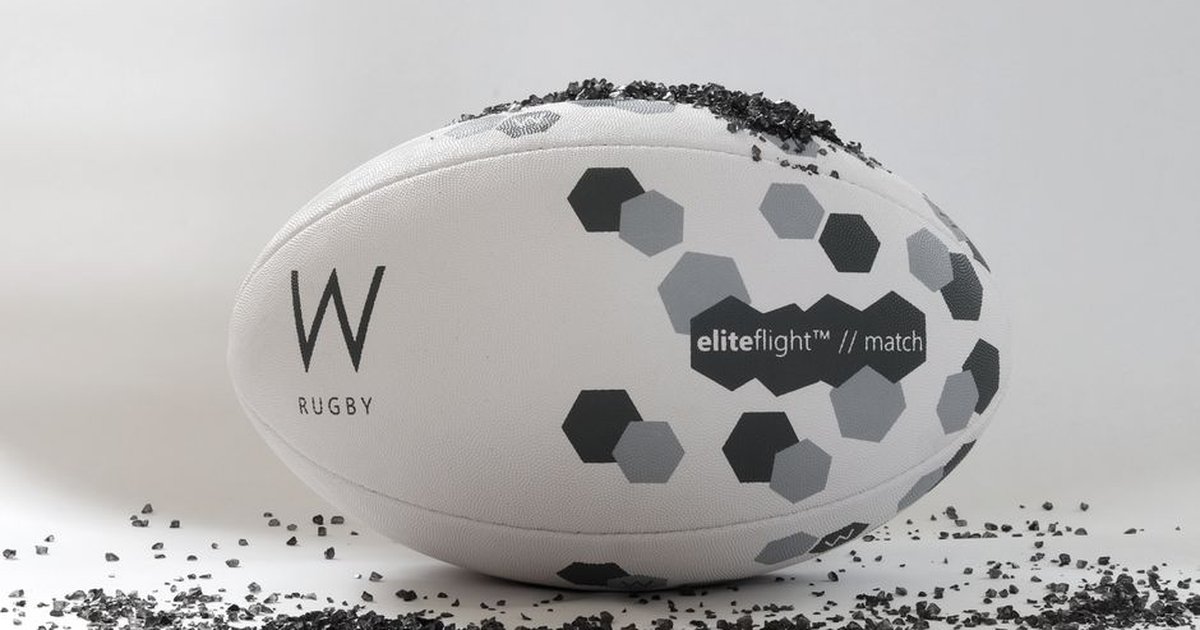 Close-up of a W rugby ball featuring hexagonal patterns on a clean, white background with scattered black granules.