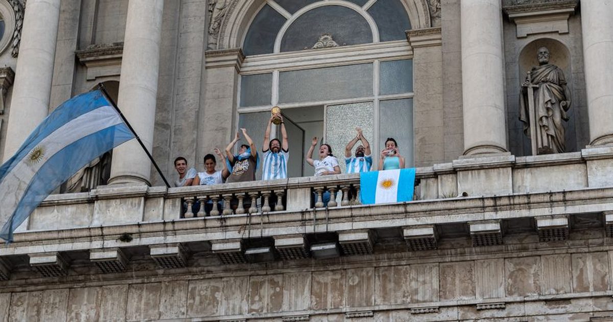 People celebrating with flags and a trophy on a Buenos Aires balcony.