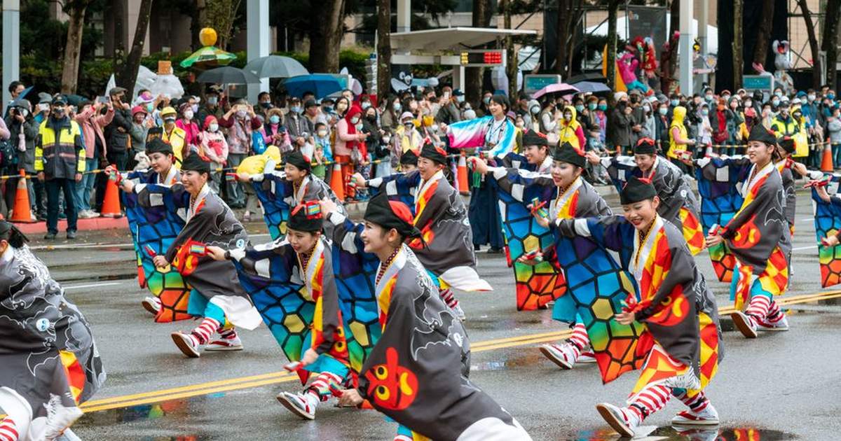 Asian women in colorful traditional clothing perform in a lively street parade.