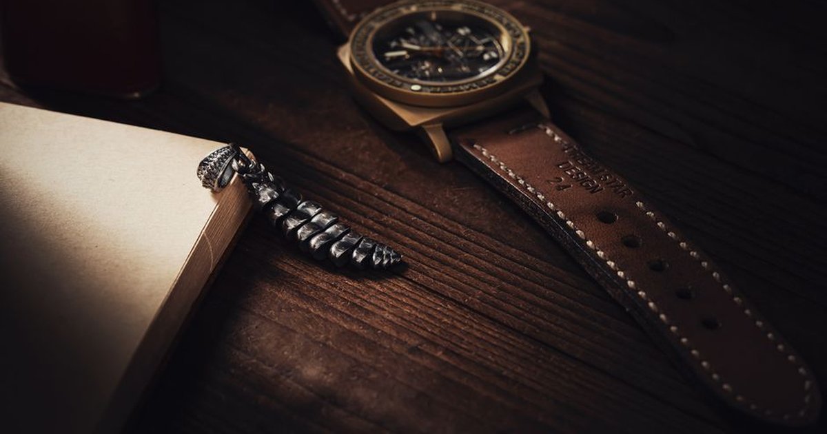 Close-up of an elegant watch and rattlesnake pendant on a wooden desk, capturing luxury and style.