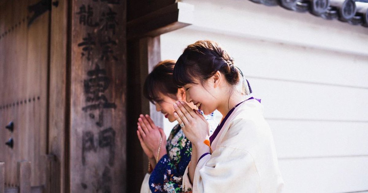 Two women in kimonos praying at a Kyoto temple gate, embracing Japanese tradition.
