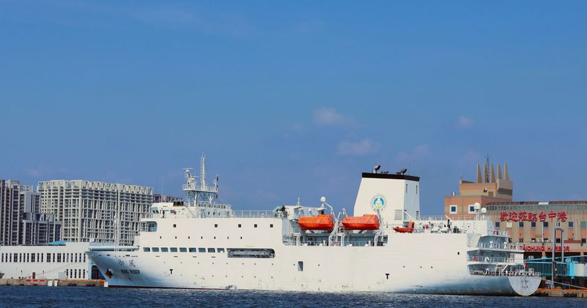 A large white ship with orange lifeboats docked at Taichung Harbor, under a clear blue sky.