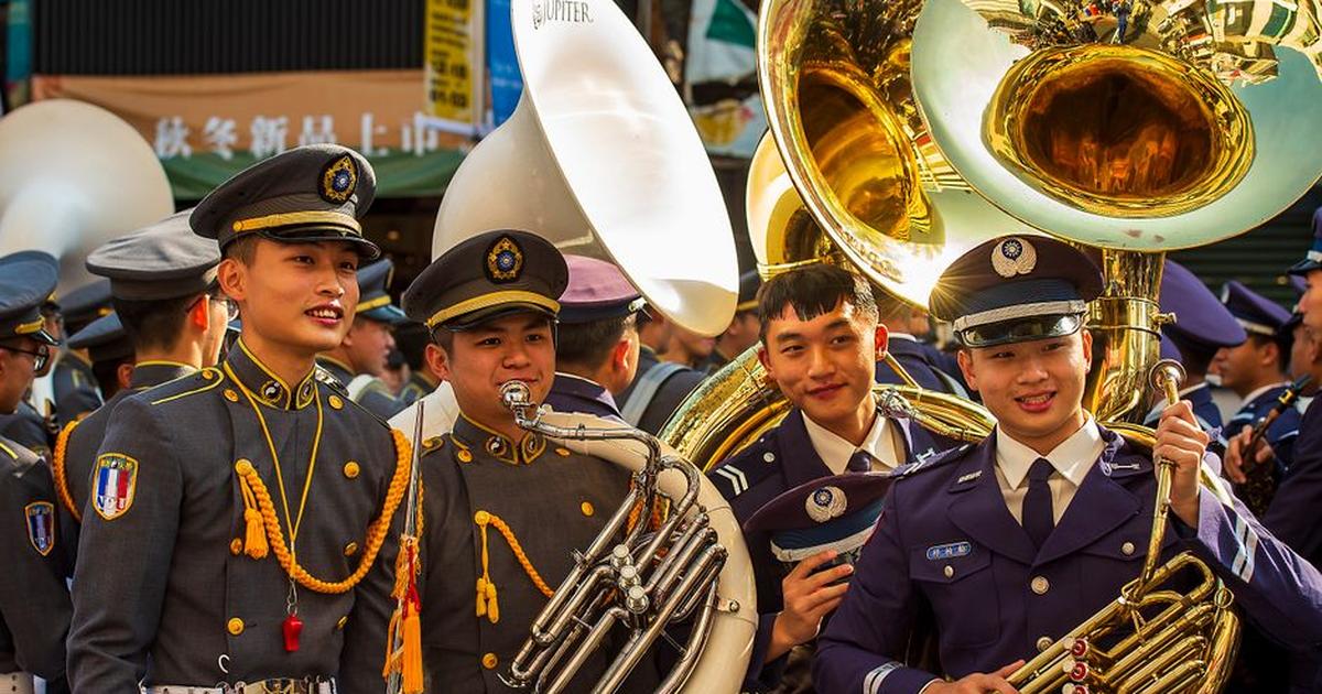 Smiling military band members in uniform playing brass instruments outdoors in Taiwan.