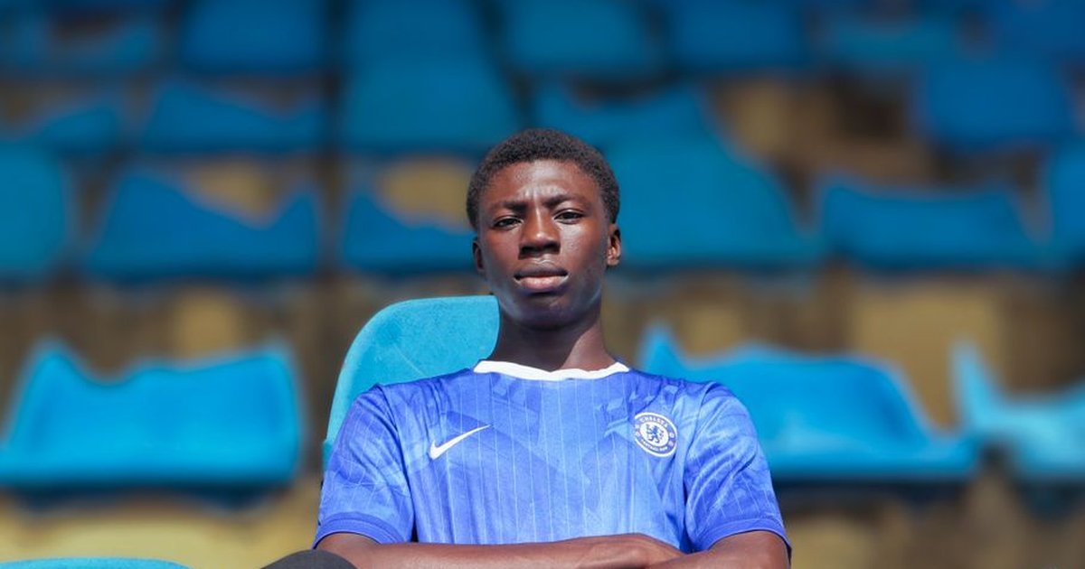 A young man wearing a blue jersey sits confidently in a stadium with blue seats in Nigeria.