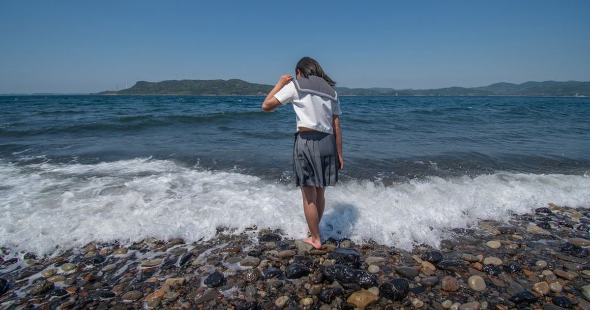 Young girl touching the waves on a pebble beach in Nagasaki, Japan.
