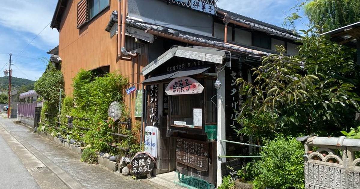 A charming traditional Japanese building on a sunny street, surrounded by greenery.