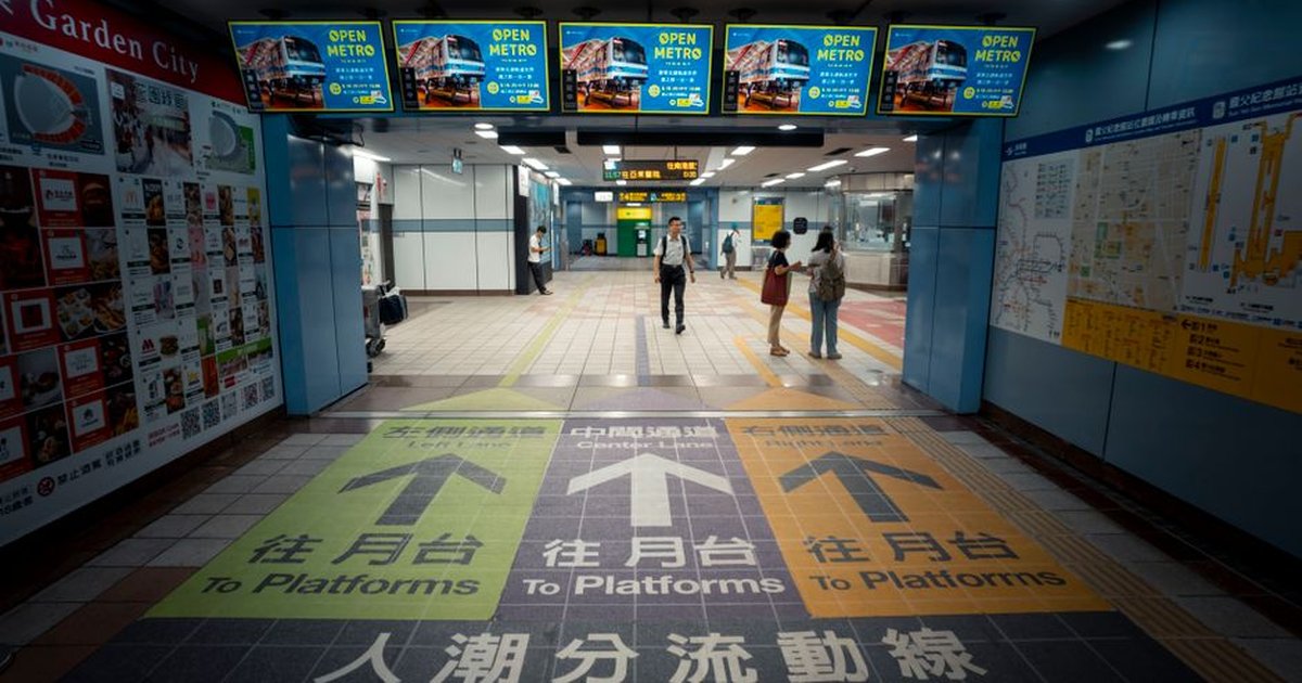 Directional arrows guide commuters at a bustling Taipei metro station entrance.