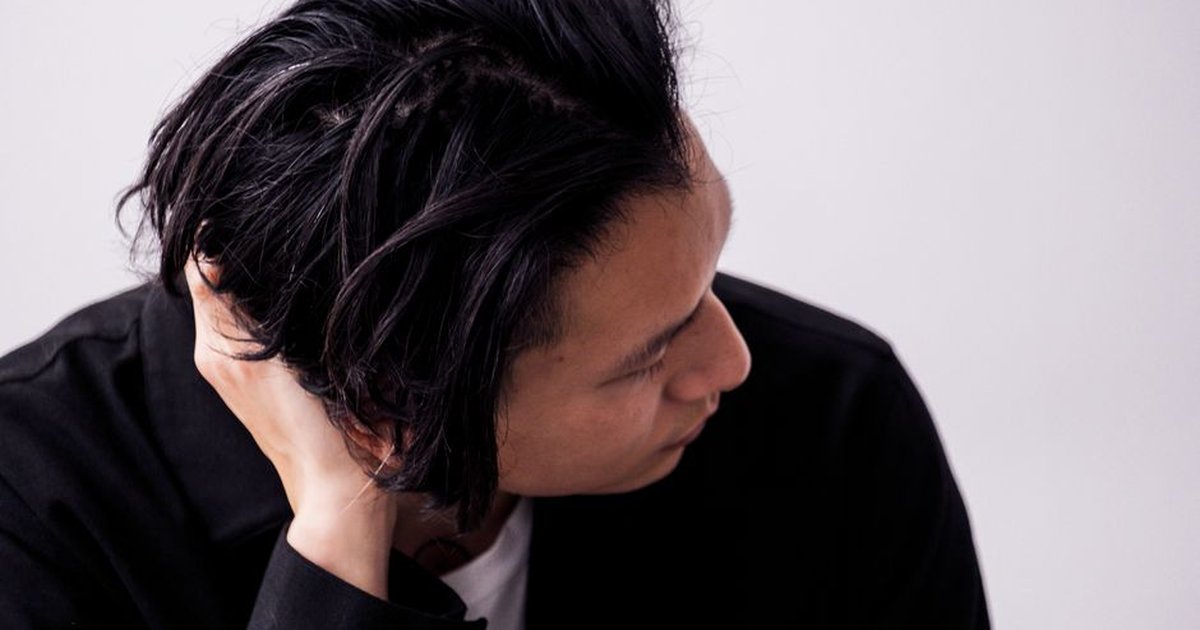 A thoughtful portrait of a man with black hair fixing his hair in a studio setting.