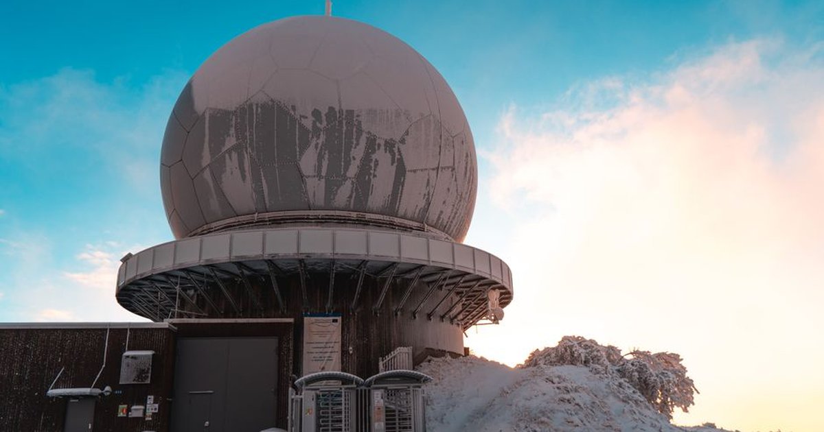 A snowy landscape featuring the iconic Radom Wasserkuppe observatory with a blue sky backdrop.