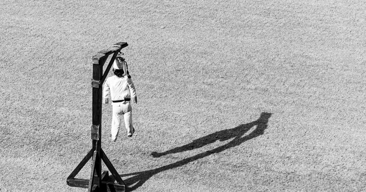 Striking black and white image of a figure hanging from a framework casting a shadow on the ground.