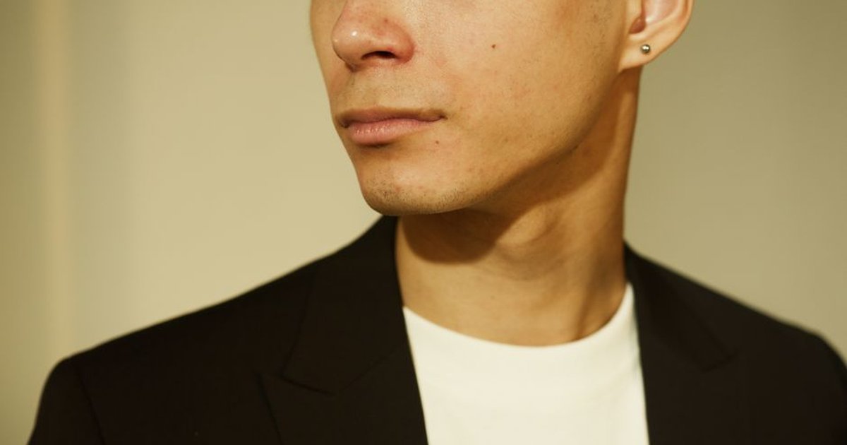 Close-up portrait of a man in a black suit looking to the side, indoors.