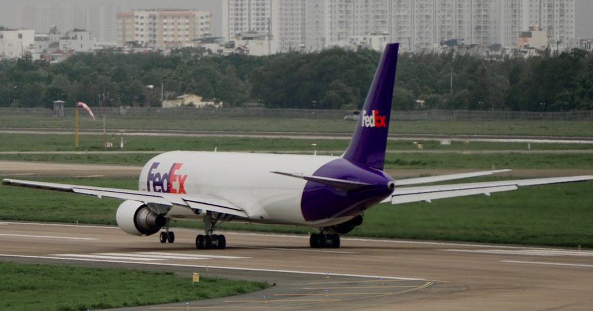 FedEx cargo plane on the runway, preparing for departure with cityscape in the background.