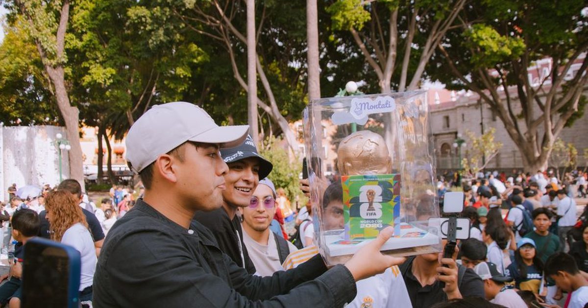 Group of people celebrating with a FIFA World Cup trophy replica in a vibrant outdoor setting.