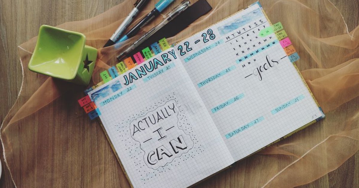 Open planner with motivational quote and colorful tabs on wooden desk.