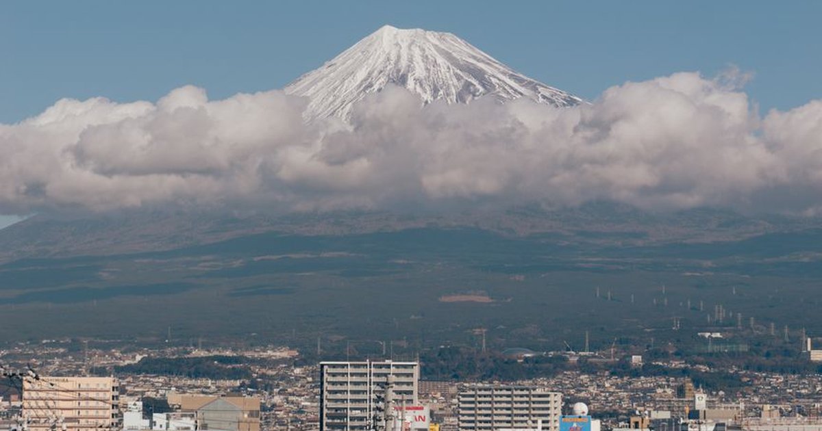 Scenic view of Mount Fuji surrounded by clouds with a cityscape in Shizuoka, Japan.