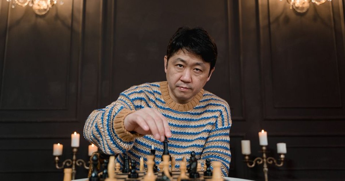 A man strategizes intensely over a chess board in an elegant, candlelit setting.