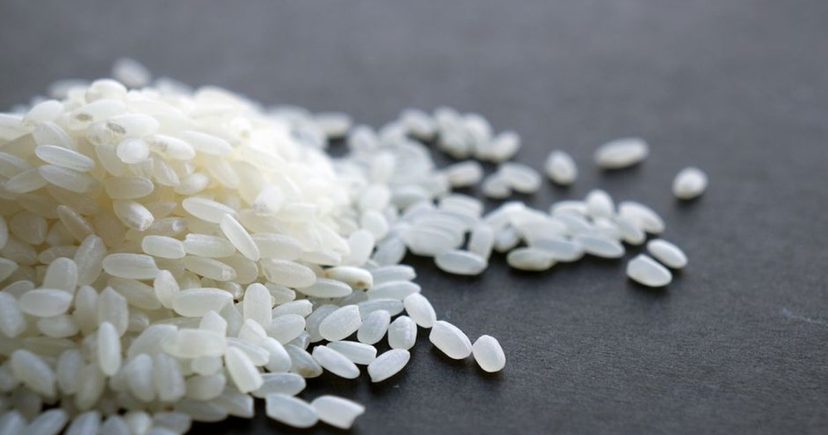 A close-up image showcasing a heap of fresh white rice grains on a dark surface.