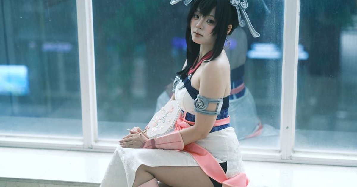 An Asian woman in elaborate cosplay seated by a window, embodying the charm of Vietnamese anime culture.