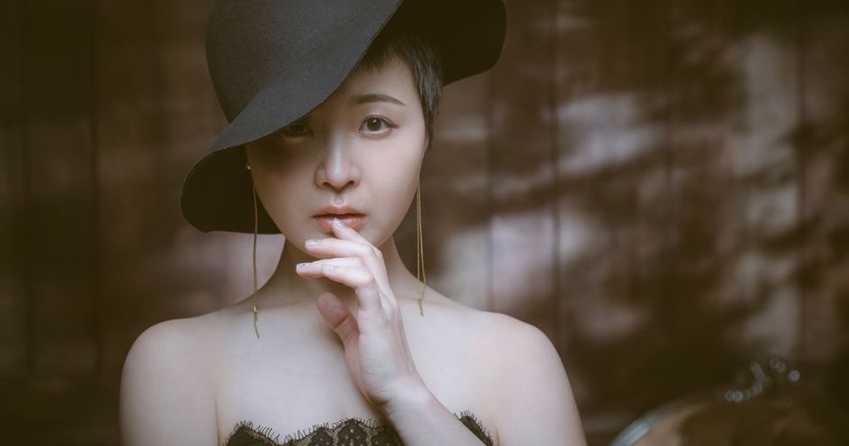 Young dreamy Asian woman in stylish clothes touching lips while looking at camera in house